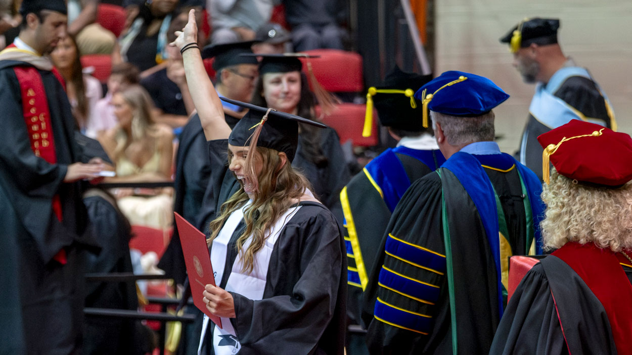 A graduate student celebrates as they cross the stage during commencement for the Ed G. Smith College of Business.