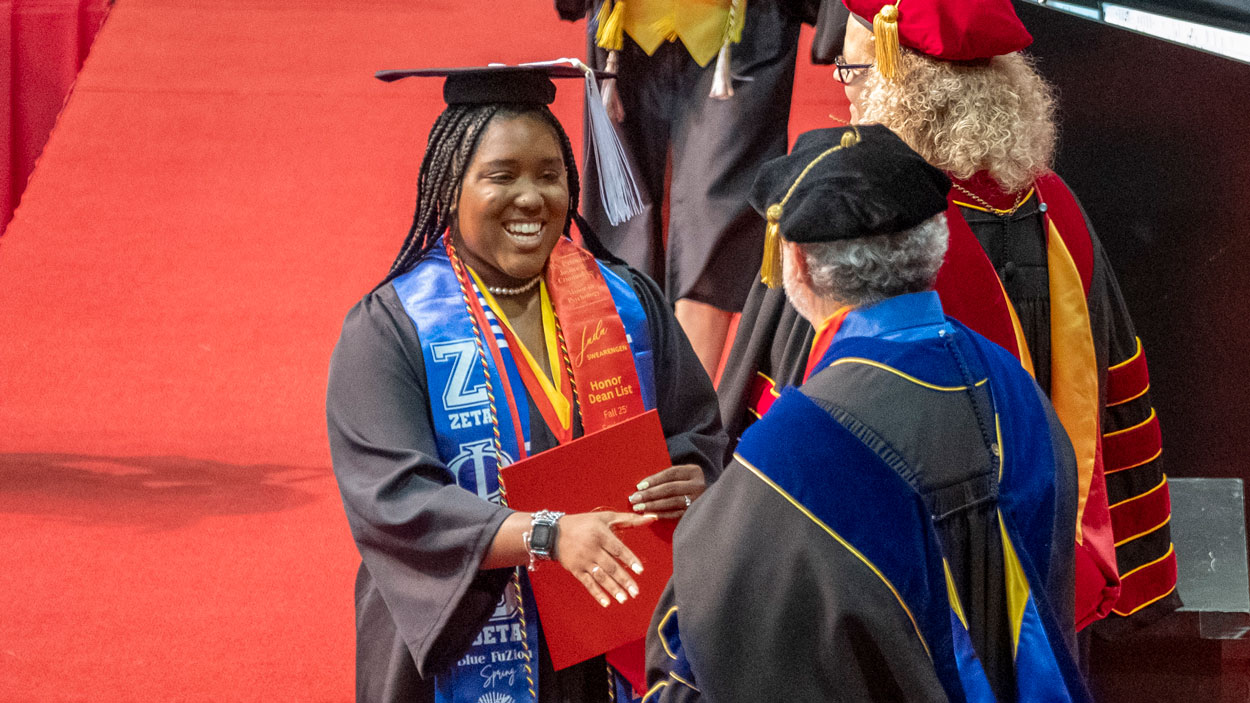 Jada Swearengen, who earned a certificate from the Pierre Laclede Honors College and a bachelor's degree in criminology and criminal justice, shakes hands with Honors College Dean Ed Munn Sanchez.