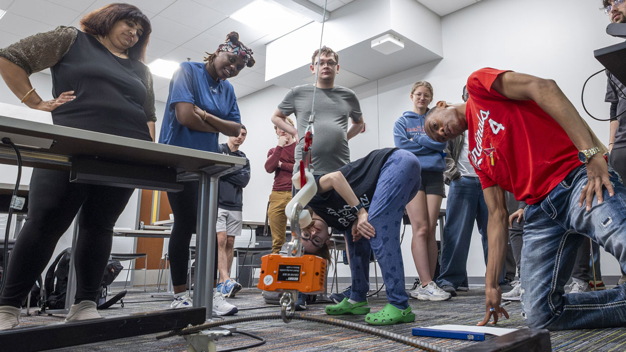 Students in the "Elementary Engineering Design" course at the University of Missouri–St. Louis School of Engineering watch as their S-Hook design is tested by holding a heavy load off the floor during a class on May 8.
