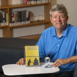 Scott D. Peterson sits with a copy of his book, "A Month of Game Days" and "The Twin Bill Book Prize for Best Baseball Fiction"