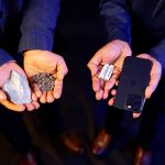 Two sets of hands hold minerals, batteries and a cellphone