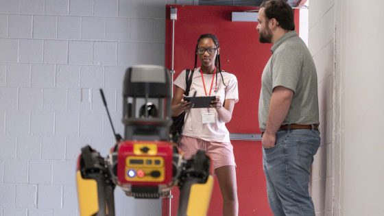 Jennings Senior High School student Jaila Owens operates the controls for Titan, UMSL's agile mobile robotic dog, as lab manager Zach Ridings waits nearby.